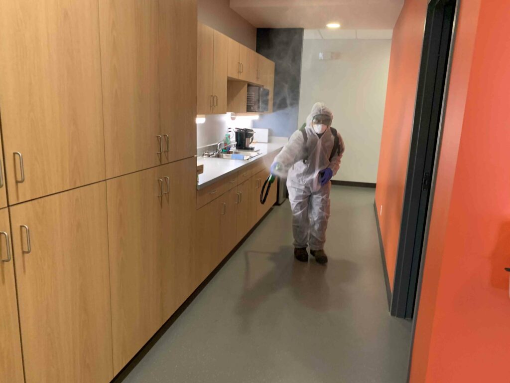 Man in PPE suit sanitizing the hallway
