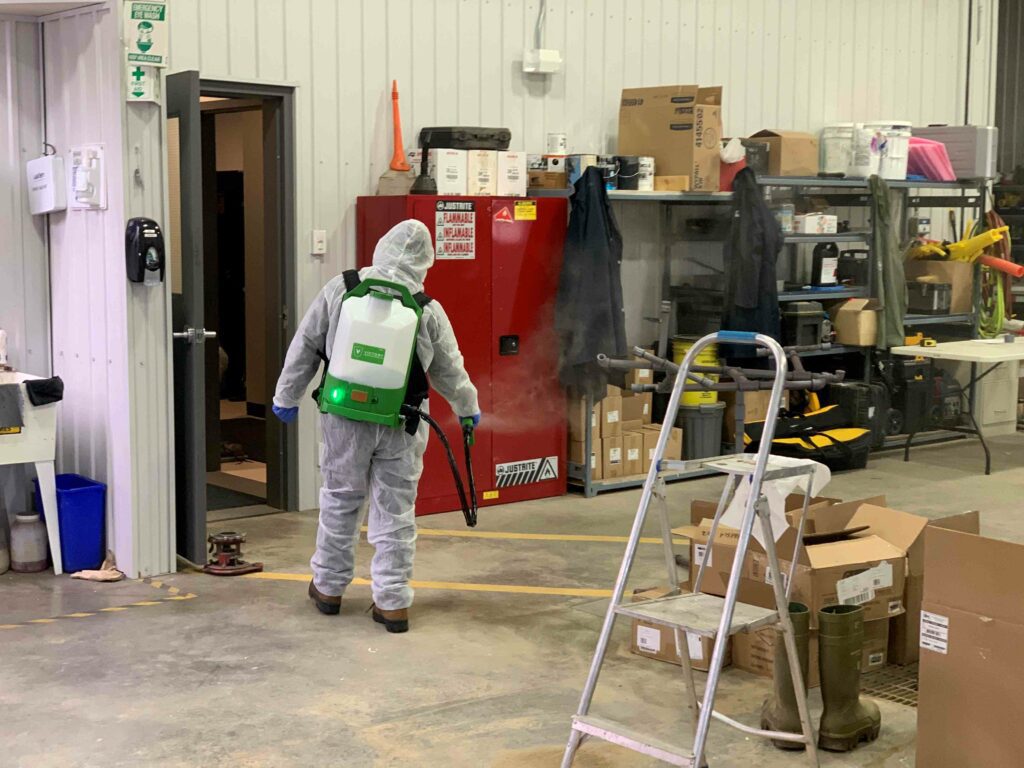 A man in PPE suit with a spraying device