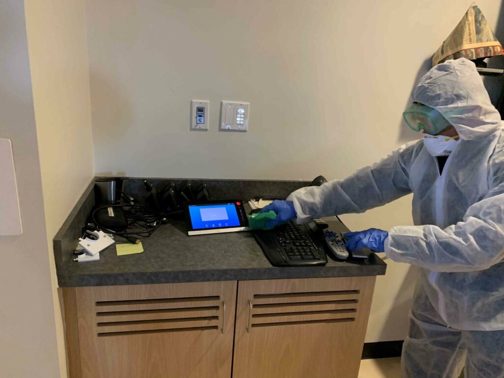 A man in PPE suit cleaning the computer peripherals